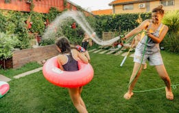 Photo of a couple of kids and their mother, having fun and refreshing with a hose on a hot summer da...