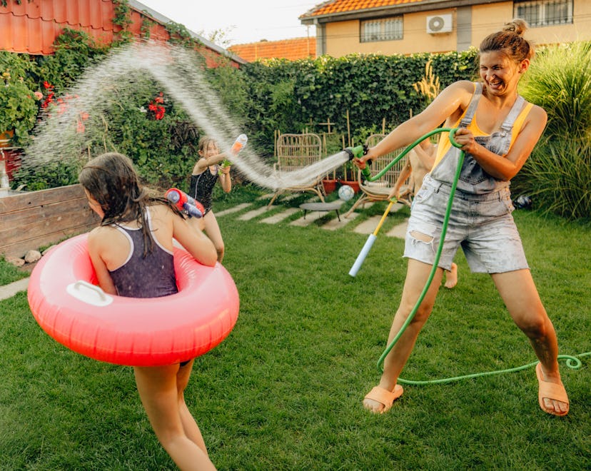 Photo of a couple of kids and their mother, having fun and refreshing with a hose on a hot summer da...