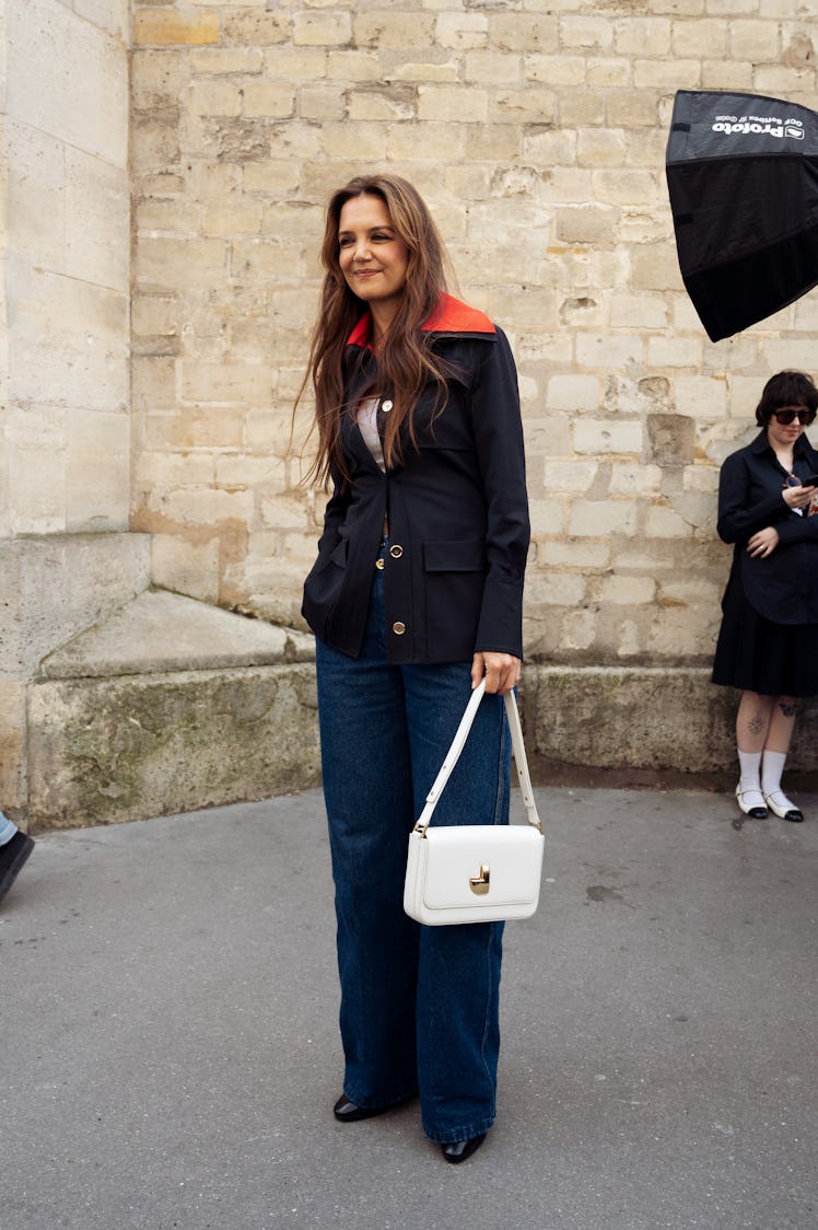 Katie Holmes wears a navy blue and red jacket, dark blue denim jeans, black shoes and a white bag ou...