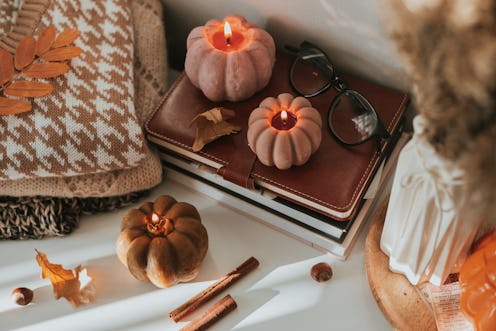 Burning candles shape of pumpkin, stack knitted season sweaters, daily and autumn leaves. Cozy autum...