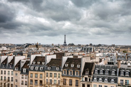 A captivating view of Paris under a cloudy sky, featuring the iconic Eiffel Tower rising above the u...