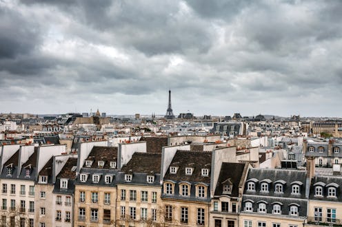 A captivating view of Paris under a cloudy sky, featuring the iconic Eiffel Tower rising above the u...