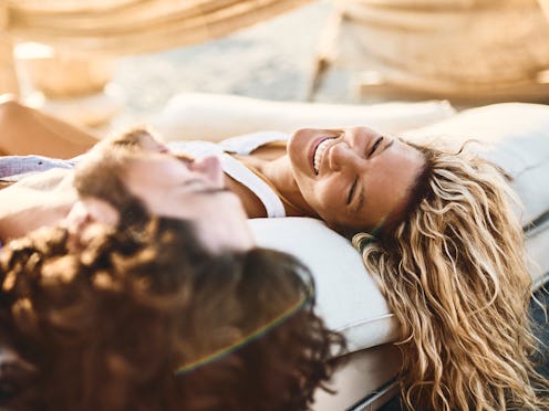 Young cheerful couple talking while relaxing on a beach bed in summer day.