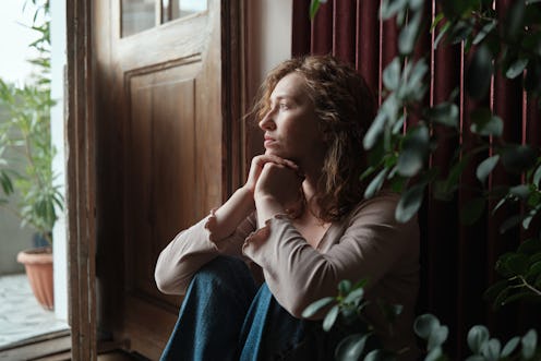 Sad depressed woman sitting on floor looking out window feeling lonely. Gen z and depression, mental...