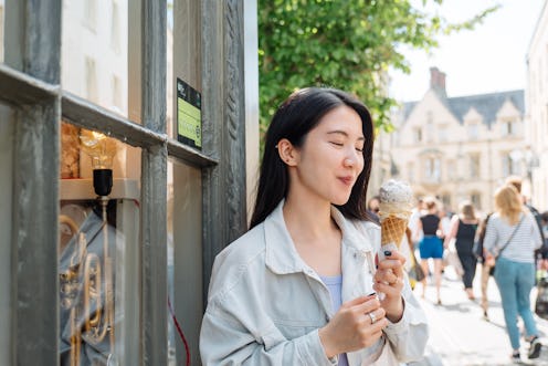 Young Asian woman enjoying ice cream on city street on a sunny summer day.