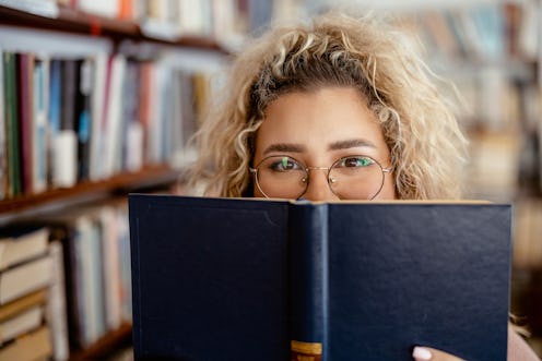 Portrait of Smiling Female College Student Hiding Her Face With a Book in Library or Book Store
