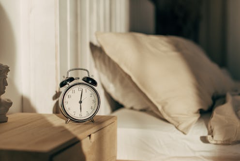 Young sleeping woman and alarm clock in bedroom at home