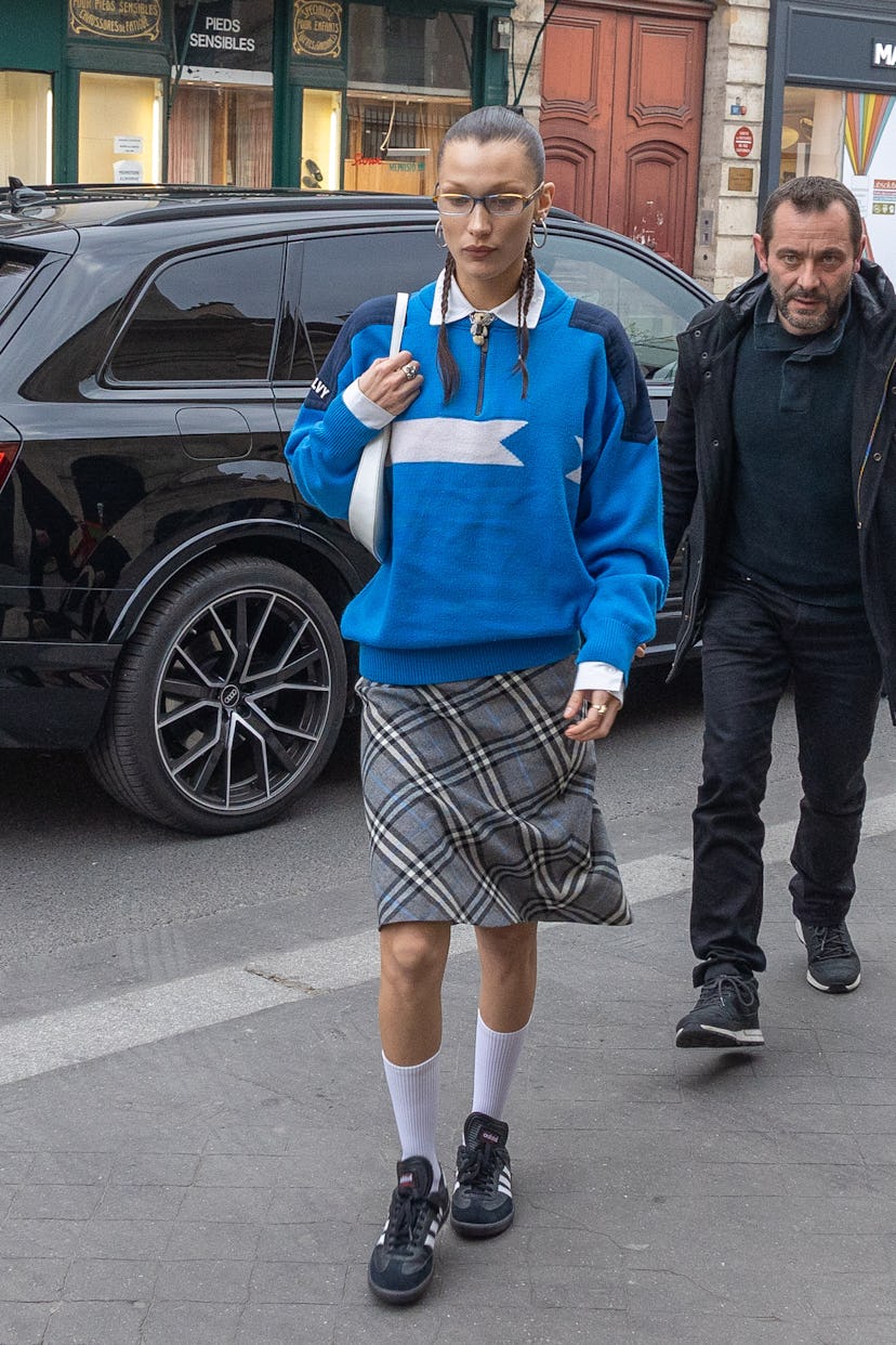 Bella Hadid wears a blue sweater, plaid skirt, and black sneakers on March 04, 2022 in Paris, France…