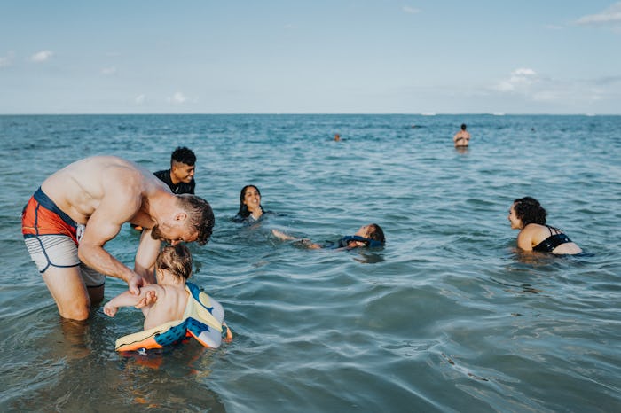 A loving Caucasian father stands in the shallow ocean and plays with his Eurasian one year old son w...