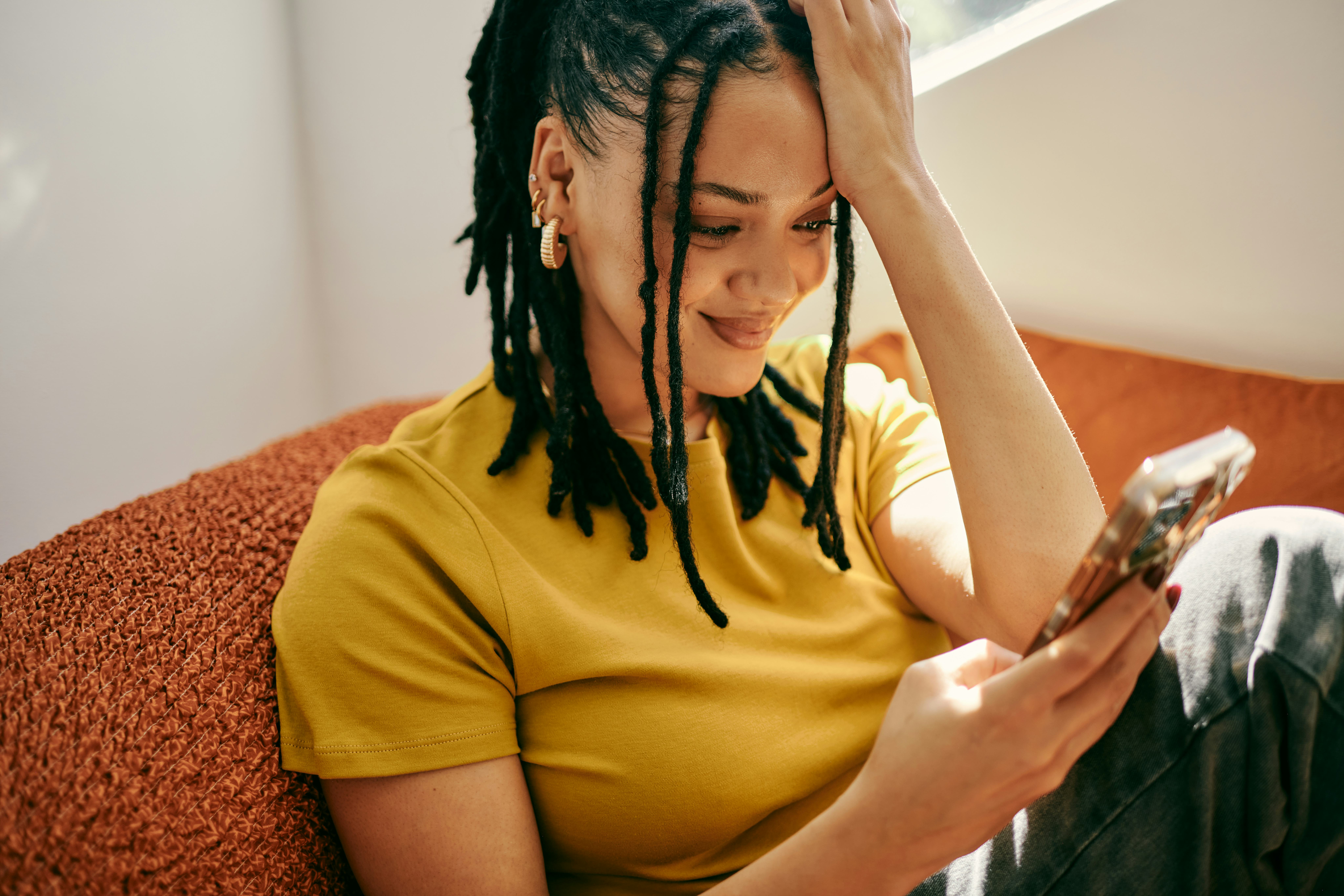 A woman sitting on her couch looking at most likely to questions on her phone
