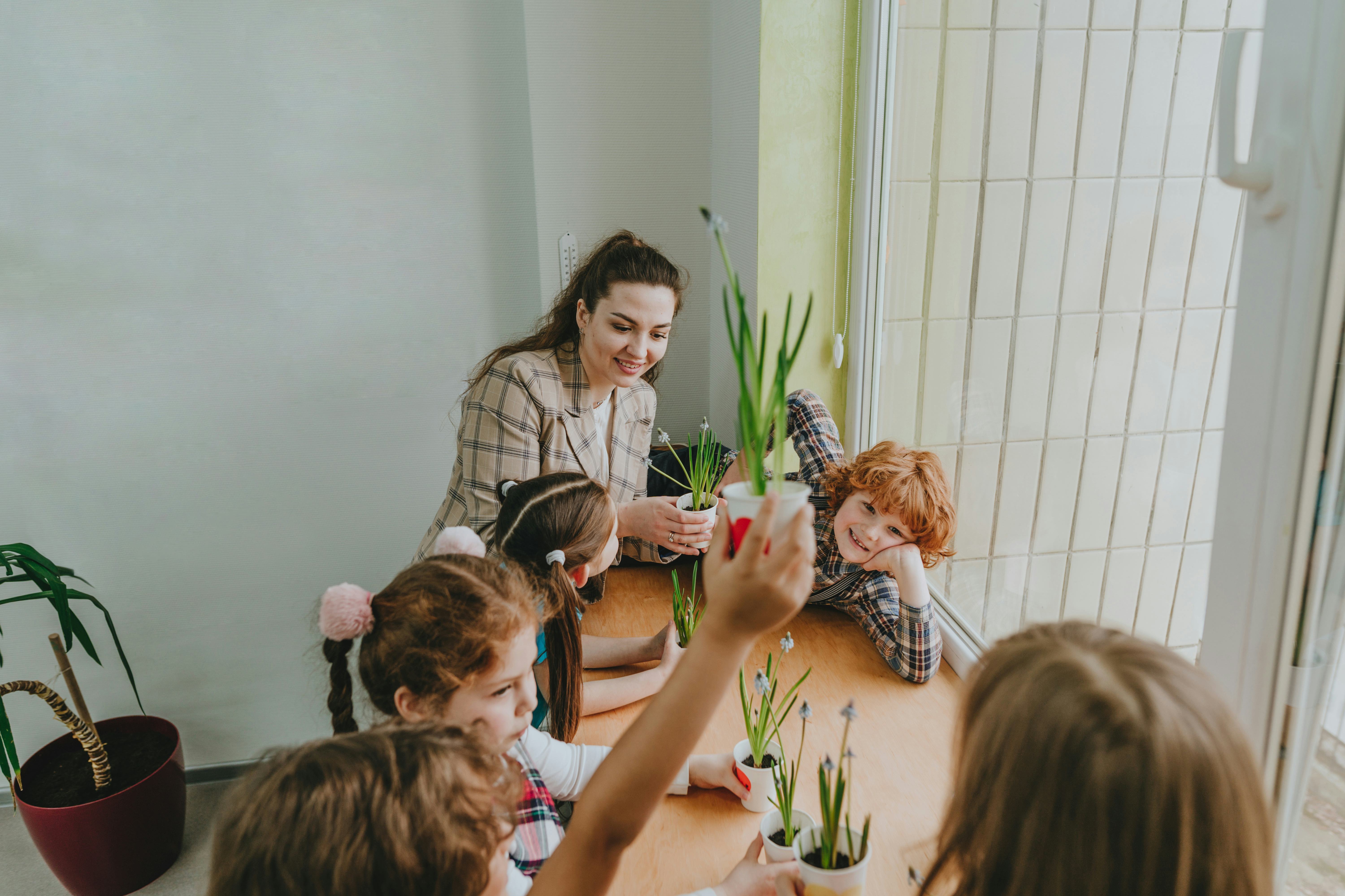 A young adult teacher telling her elementary students plant jokes by a window