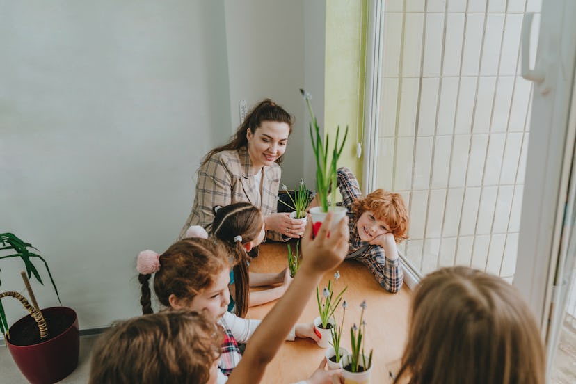 A young adult teacher telling her elementary students plant jokes by a window