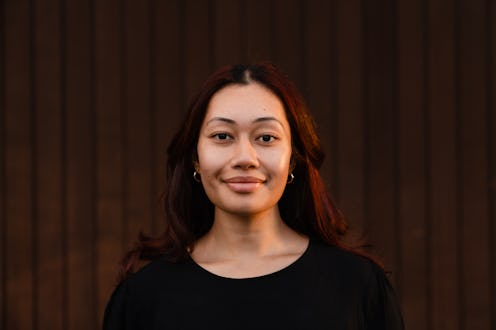 The portrait of confident smiling young woman looking at camera while standing against brown backgro...