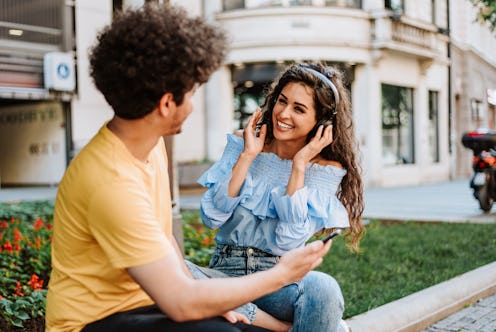 Beautiful Latino couple sitting on city street and enjoying together in a good time. They are using ...