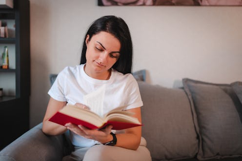 Young woman sitting on the sofa at home and reading a book.