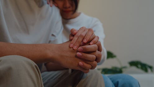 Closeup young Asian woman supporting depressed frustrated boyfriend together on sofa in living room ...