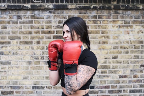 A woman boxer with tattoos smiles confidently, red boxing gloves in hand.