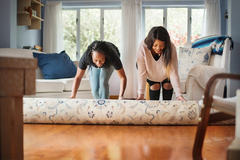Two young women unrolling a rug and laughing at some funny jokes for adults