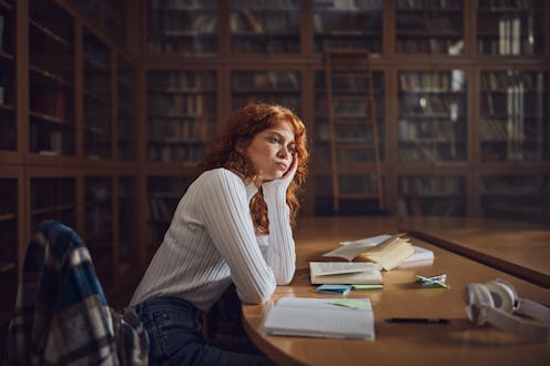 Redhead female student brainstorming while studying in library.