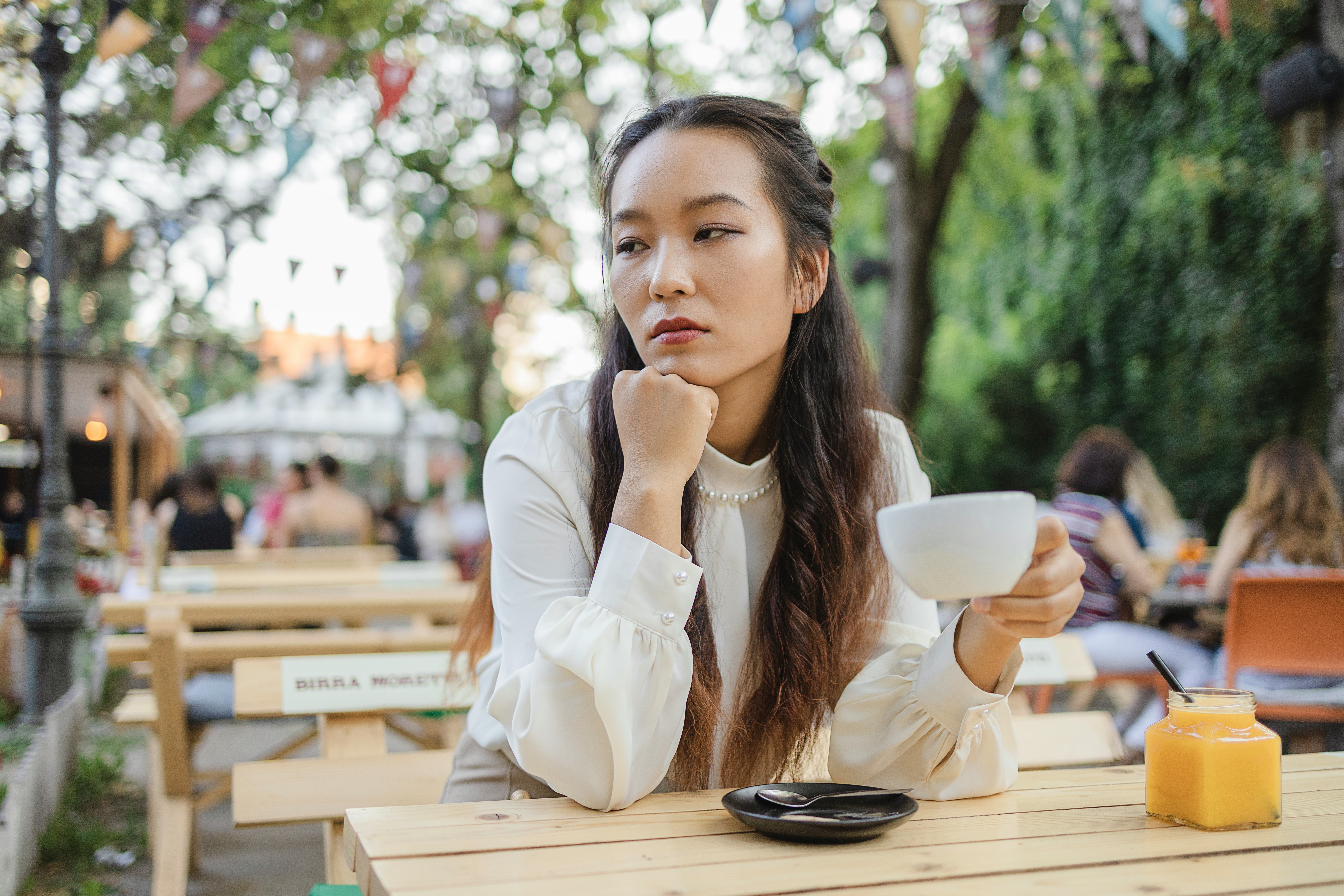 A woman sitting alone at a cafe holding a coffee cup, annoyed at a bad pickup line a man used on her