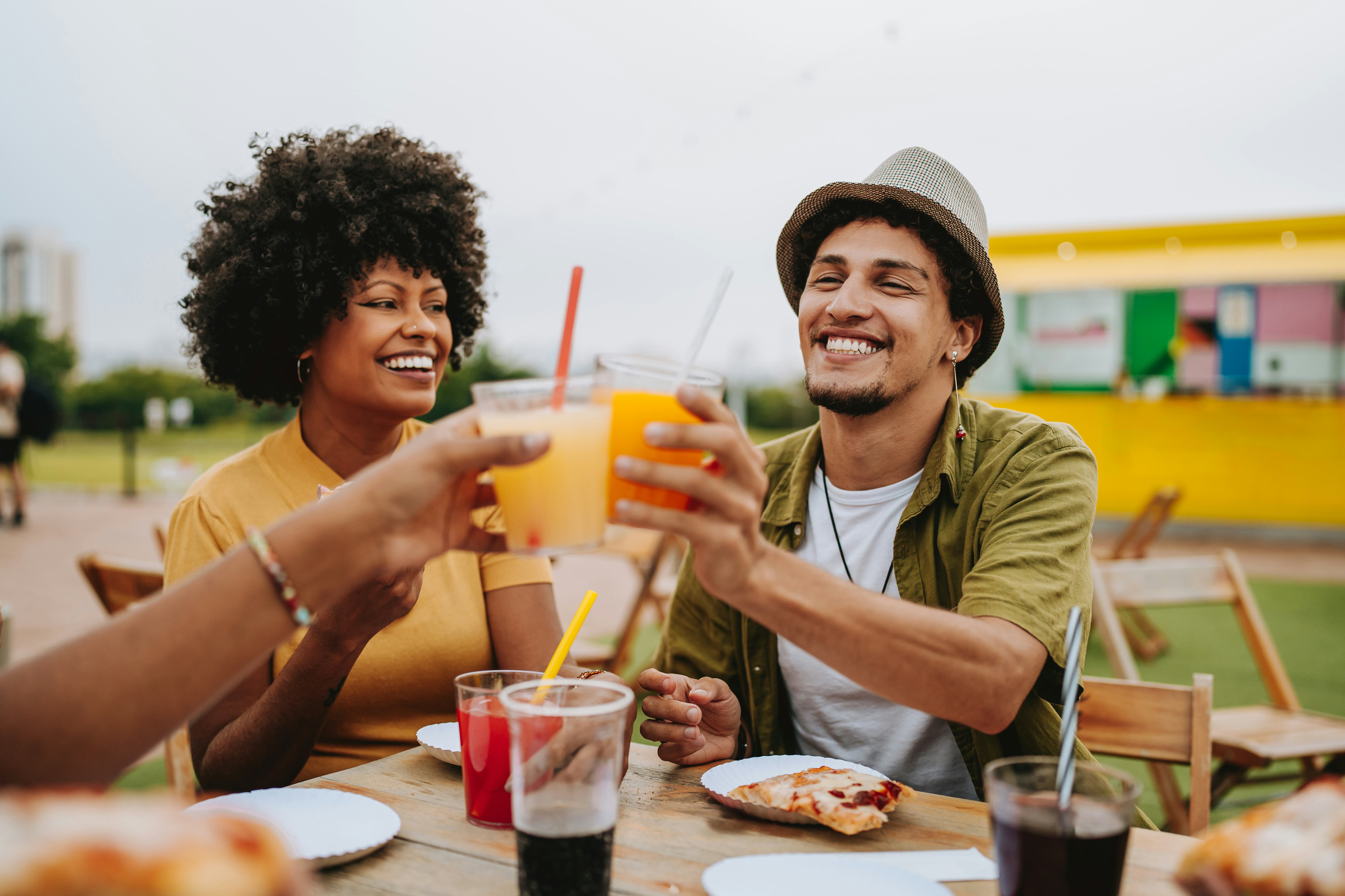 A man sitting at a table using pickup lines on a woman and doing a cheers with their drinks