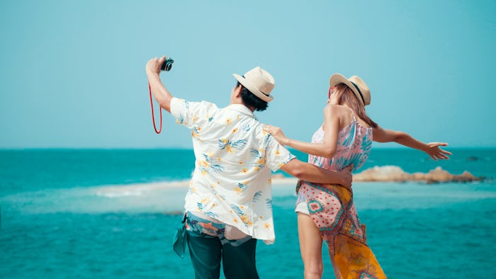 Thai couple stand on a rock at a viewpoint with an epic view of the ocean. A popular tourist destina...