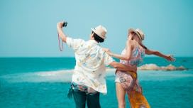 Thai couple stand on a rock at a viewpoint with an epic view of the ocean. A popular tourist destina...