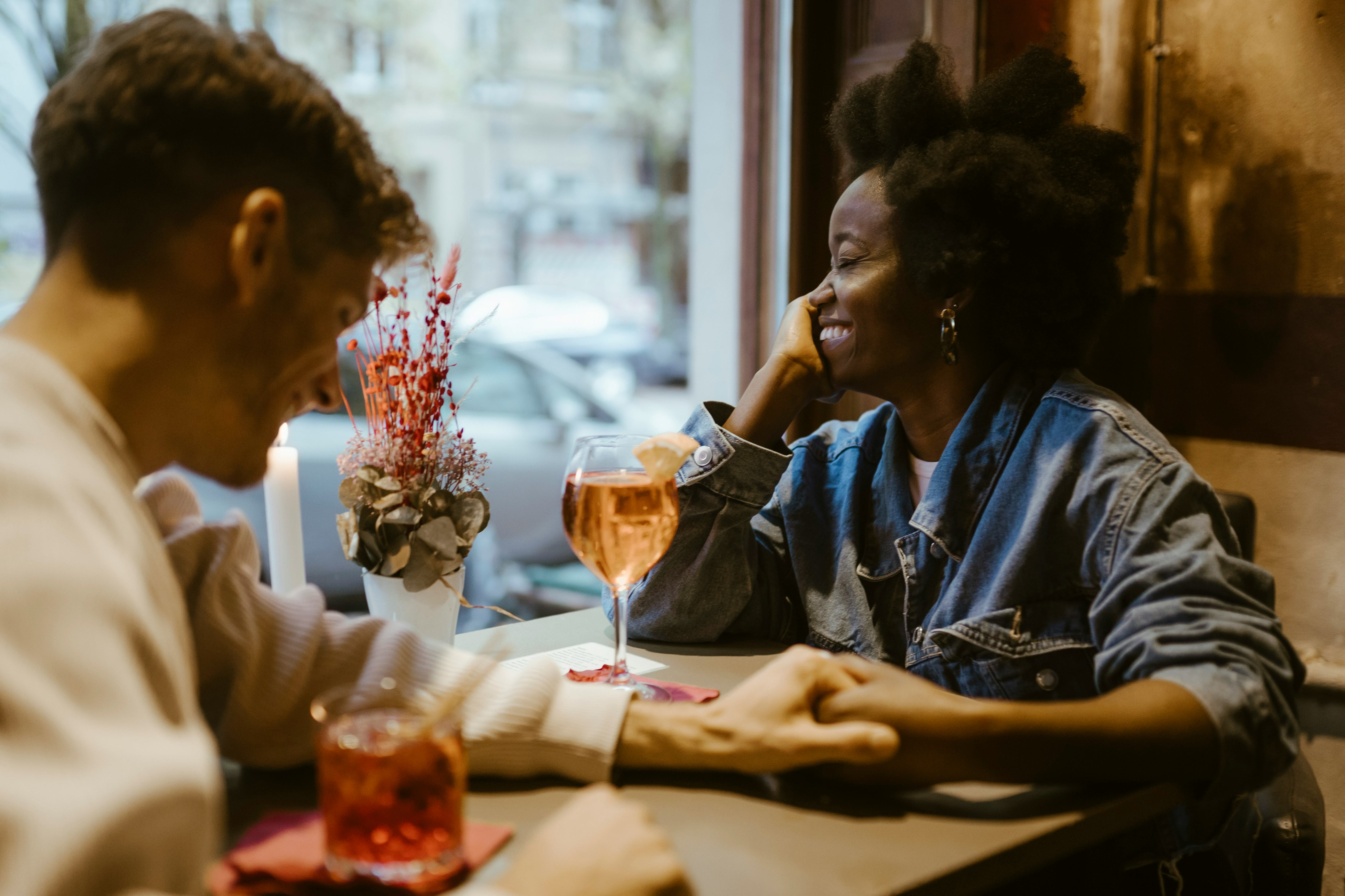 A young man using pickup lines on a woman at a bar table, holding her hand as they have drinks