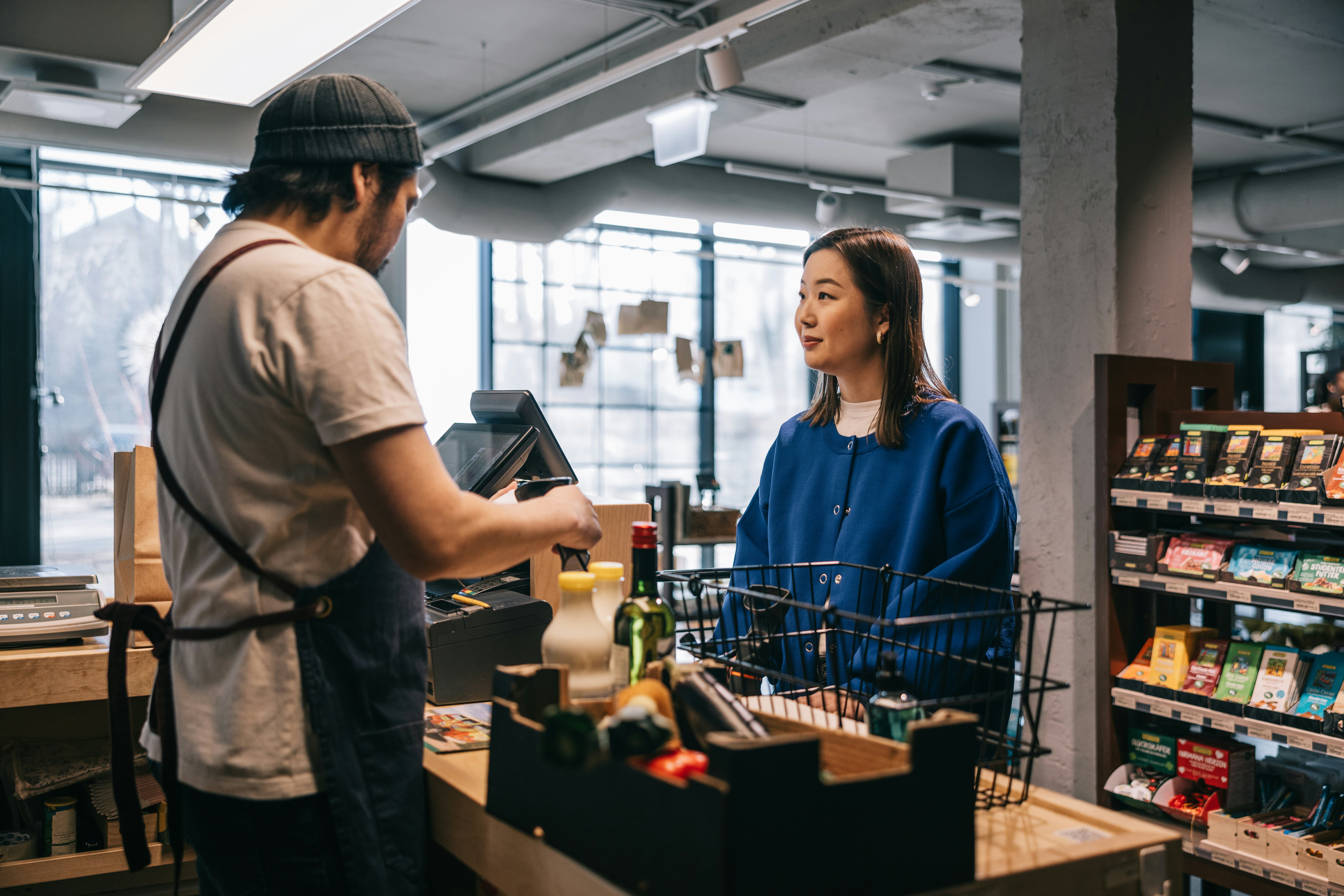 A woman standing at a grocery checkout as the clerk checks her out and uses a pickup line on her