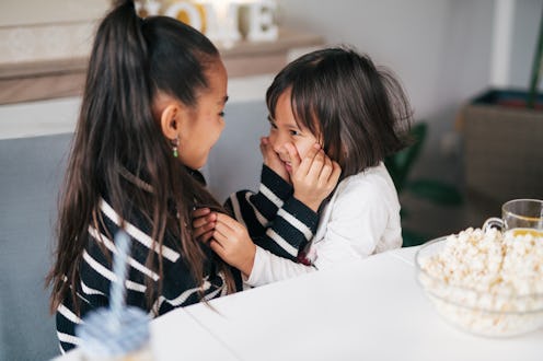 Two sisters in the dining room are having a great time together,they laughing and playing.They grab ...