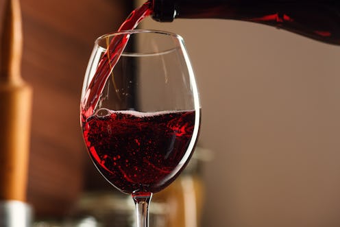 Close-up of French Red Wine Pouring into a Glass in bubbles With a Splash on the table in the kitche...