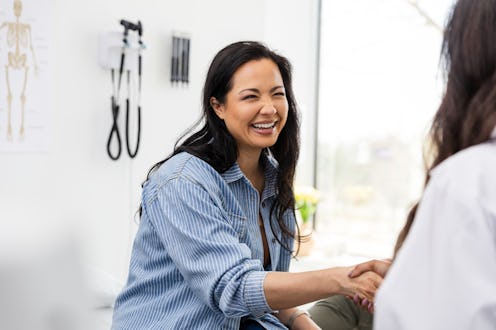 The mid adult female patient smiles and shakes hands with the unrecognizable doctor who is seeing he...