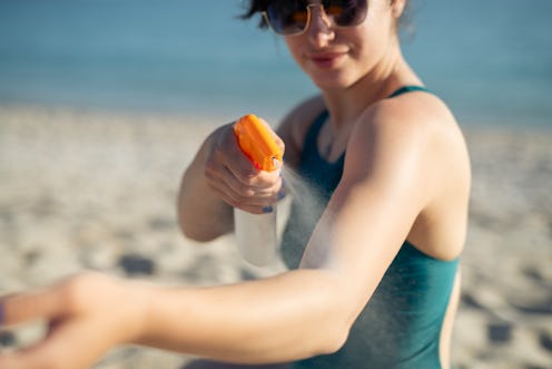 Shot of woman applying sunscreen at beach on sunny day.