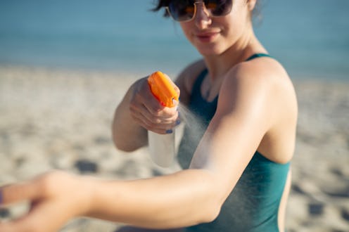 Shot of woman applying sunscreen at beach on sunny day.