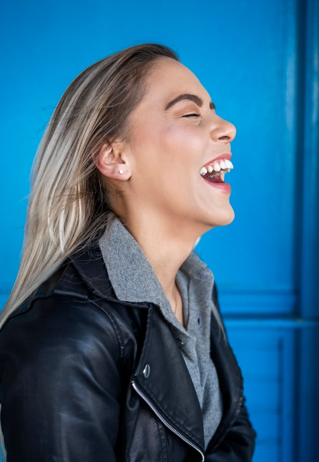 Side view of a cheerful young woman smiling against blue wall