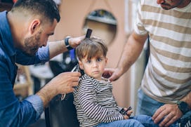 Cute little boy at the barber shop getting his first haircut with his father