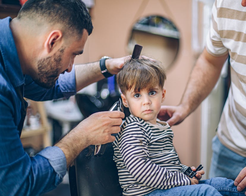 Cute little boy at the barber shop getting his first haircut with his father