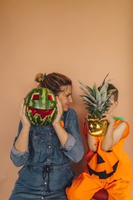 Mother and son holding a watermelon and a pineapple over their faces on a Halloween