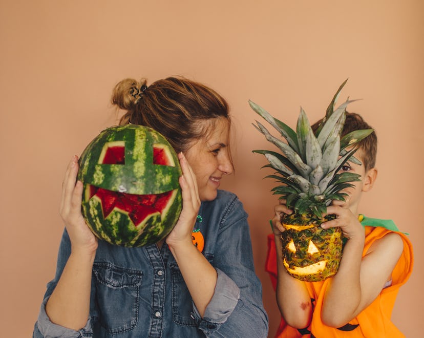 Mother and son holding a watermelon and a pineapple over their faces on a Halloween