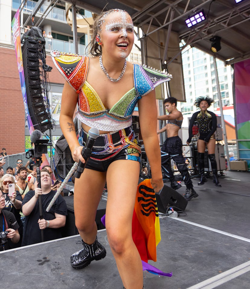 Woman in colorful costume performing at an outdoor festival, with an enthusiastic crowd and photogra...