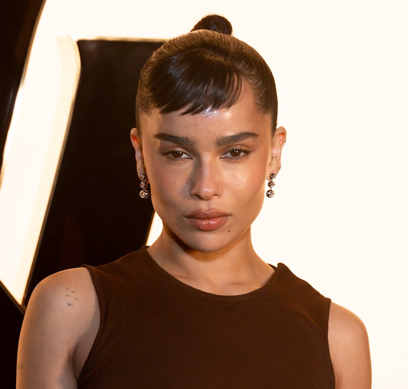 Woman with slicked-back hair and bangs poses in front of a camera light, wearing a sleeveless top an...