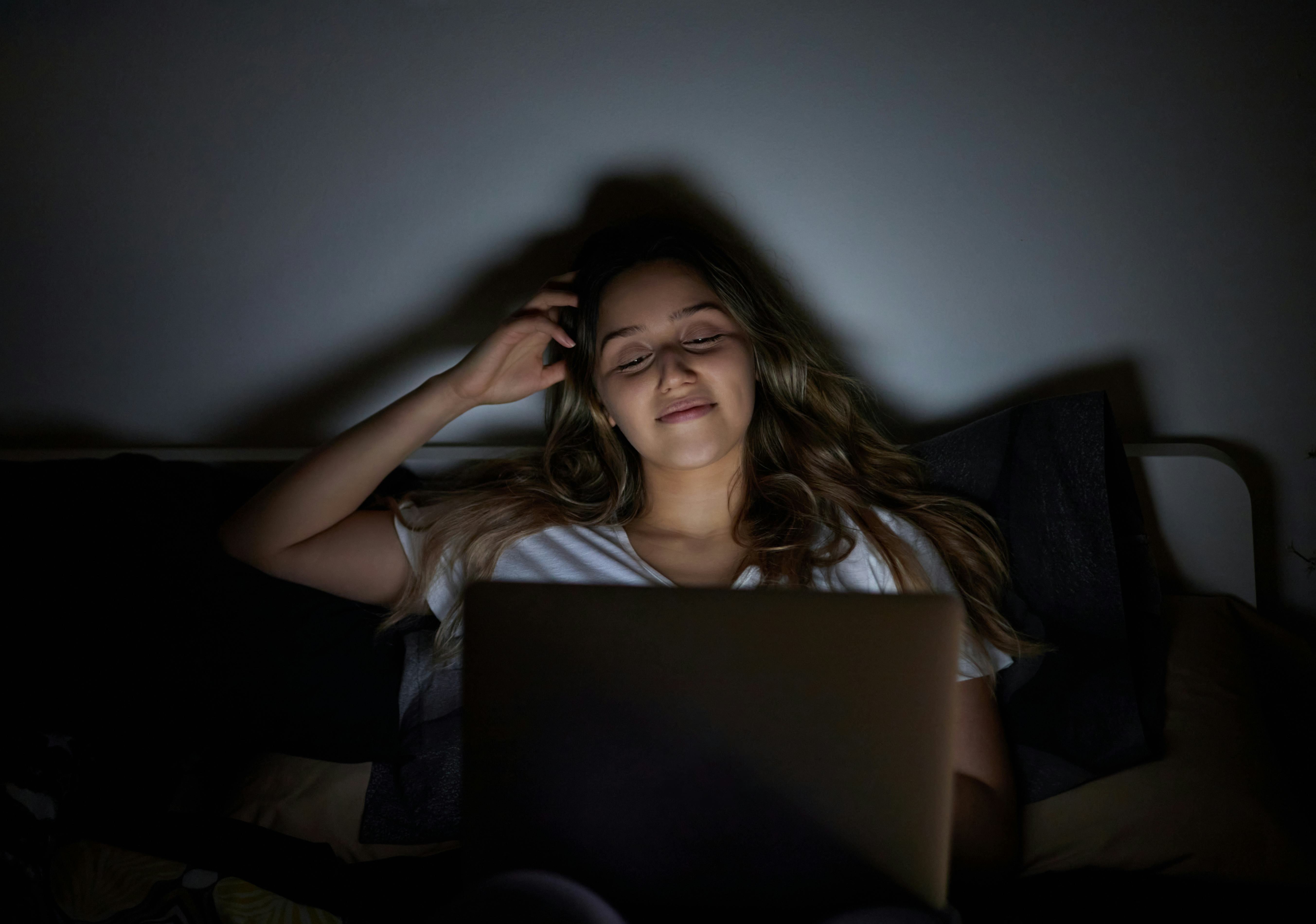 Happy and cheerful woman with laptop in her bedroom bed.
