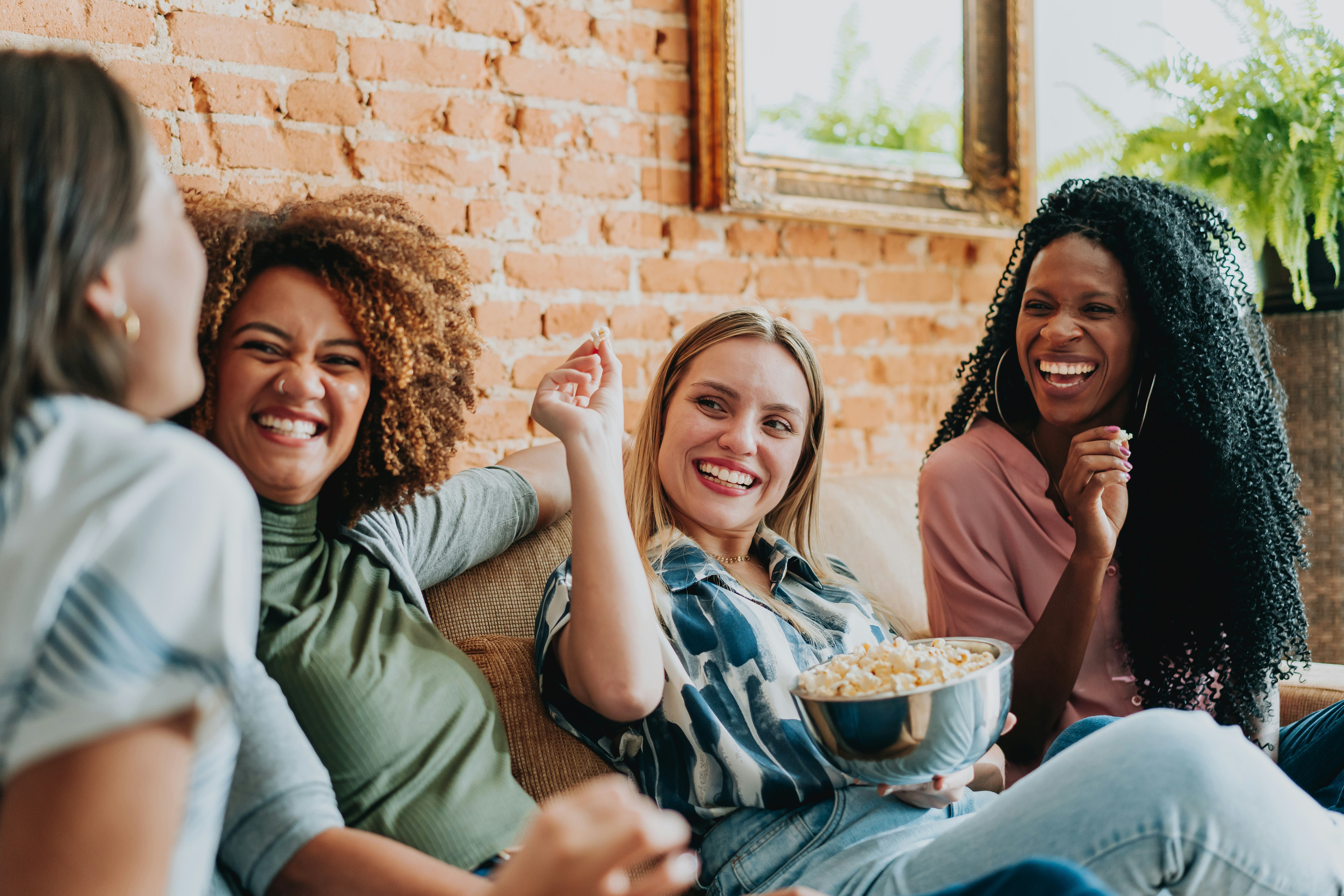 Group of female friends watching tv at home and eating popcorn