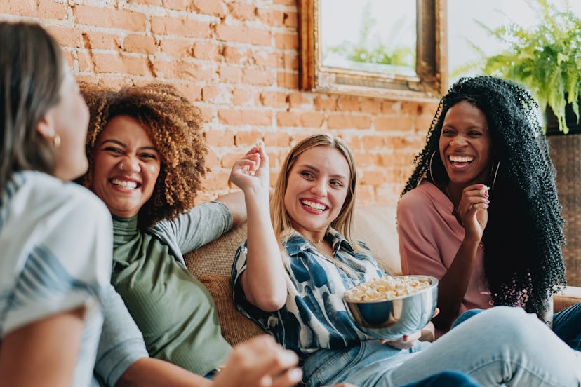 Group of female friends watching tv at home and eating popcorn