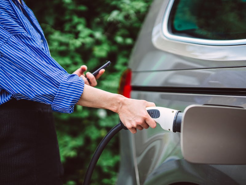 Young businesswoman charging her electric car at an EV charging station, highlighting the shift towa...