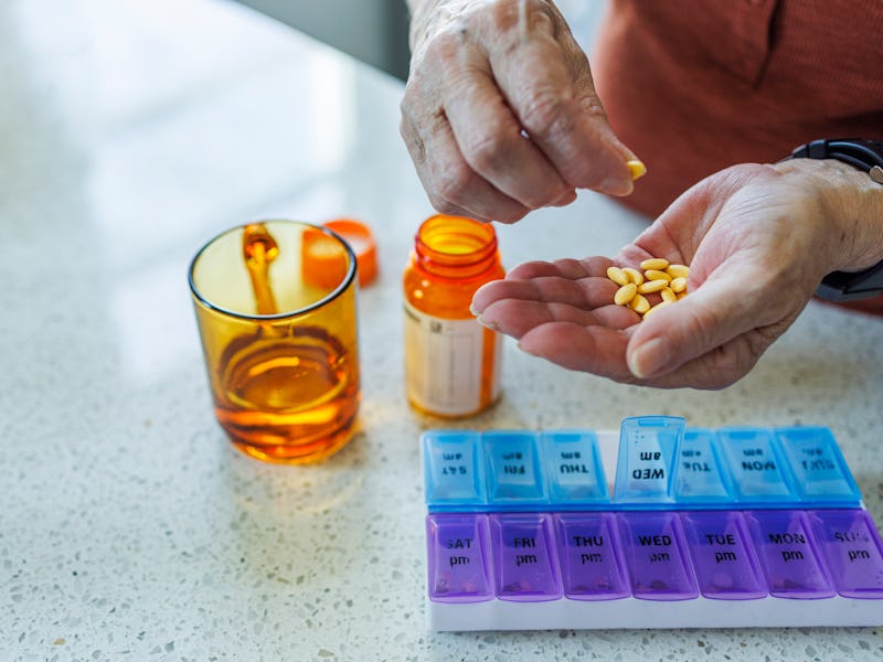 Close-up of Caucasian elderly woman's hands as she organizes her medication into daily pill organize...