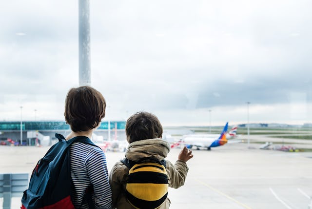 Two people, one adult and one child, look out a large airport window at planes on tarmac, child poin...