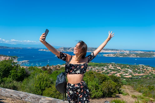 Young female tourist taking selfies from a high viewpoint above Maddalena archipelago.