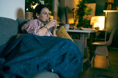 Young Caucasian woman drinking tea and watching tv during the relaxing evening at home.