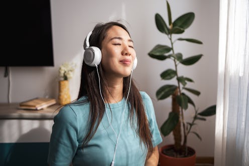 Asian woman enjoying music with headphones at home, relaxing in the living room